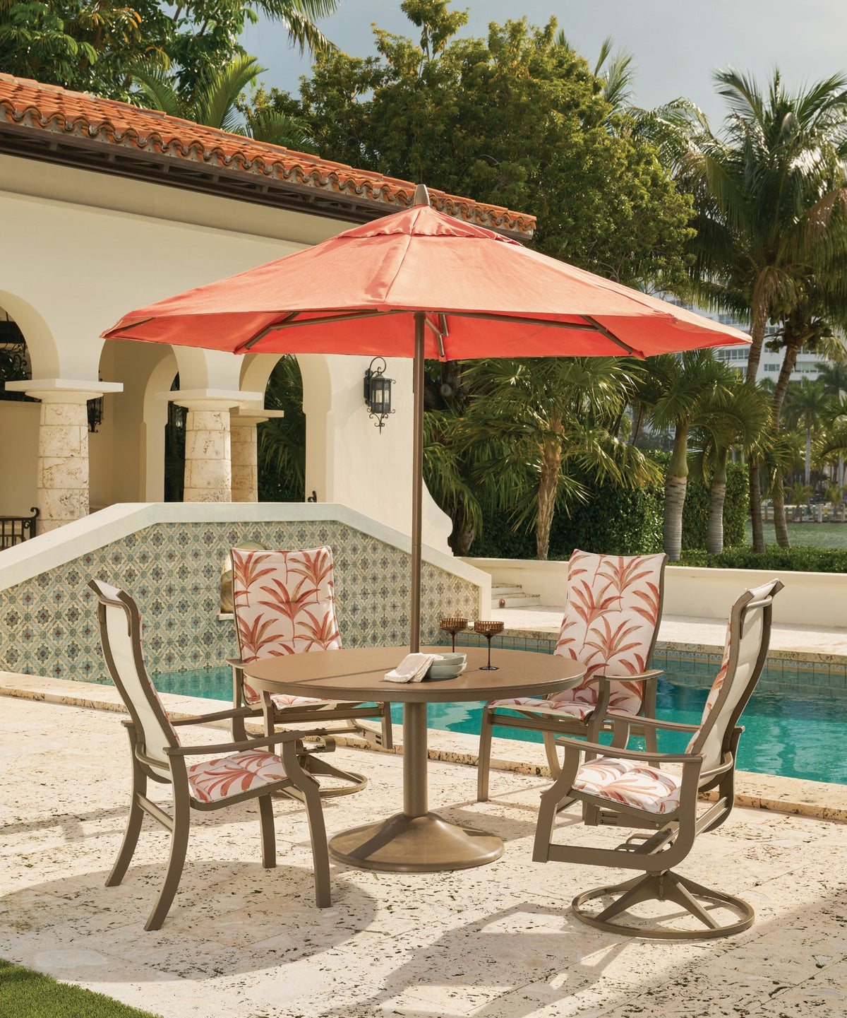 Telescope Casual Cascade dining table with swivel chairs under a coral umbrella by a pool