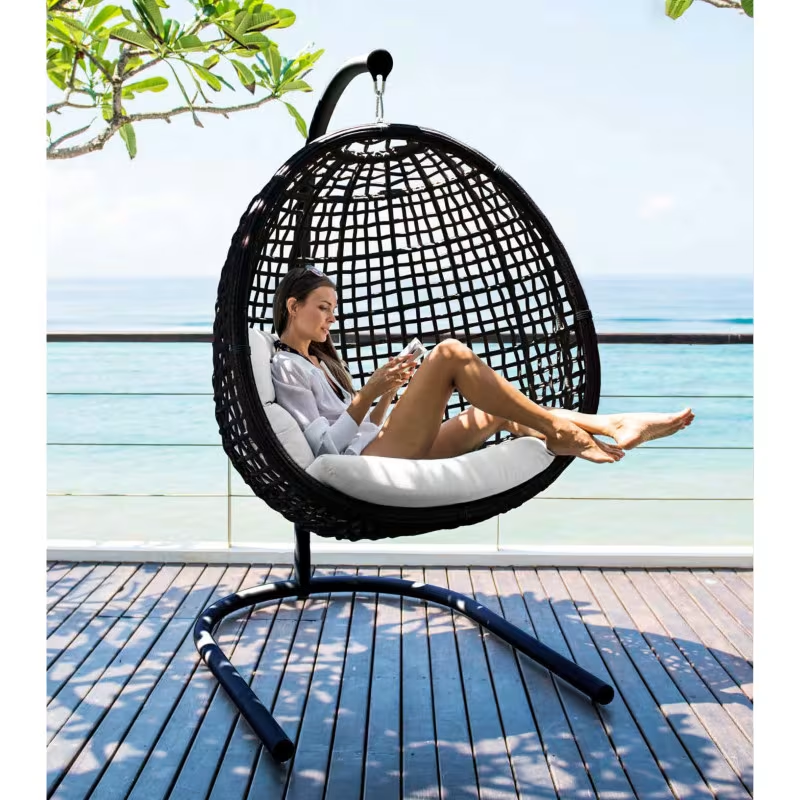Woman relaxing in a black Skyline Design Dynasty hanging egg chair on a seaside deck