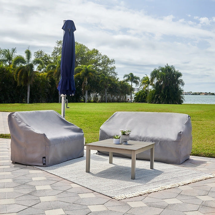 Telescope Casual Weather Max covers on an outdoor lounge chair and loveseat on a waterfront patio, beside a closed navy umbrella