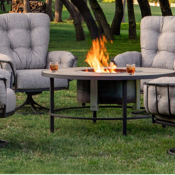OW Lee Monterra swivel rockers around a fire table on a lawn under oak trees