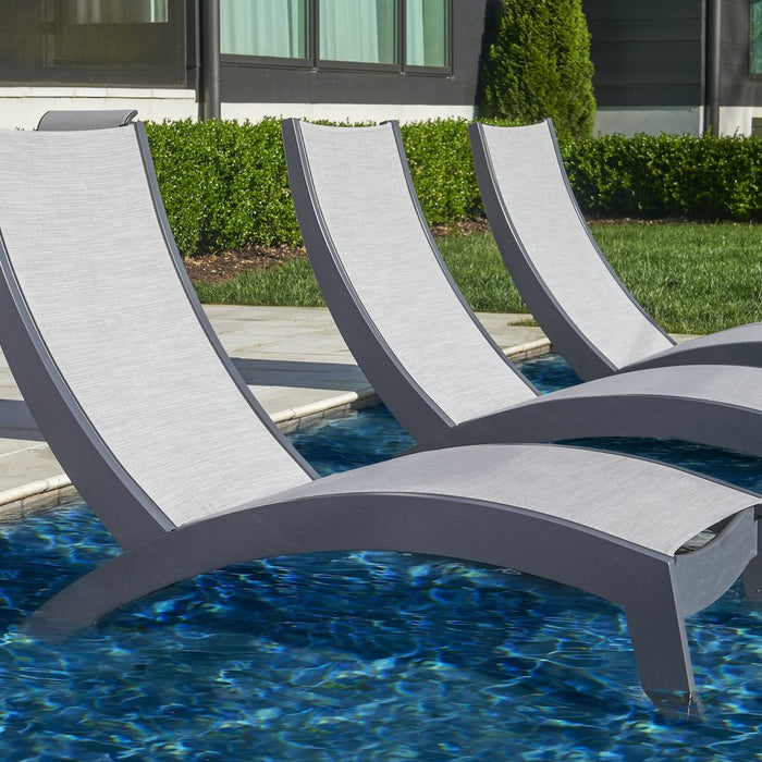 Three Telescope Casual Dune MGP Hydro-Lounge chaises with gray frames and slings sitting in the shallow water of a pool