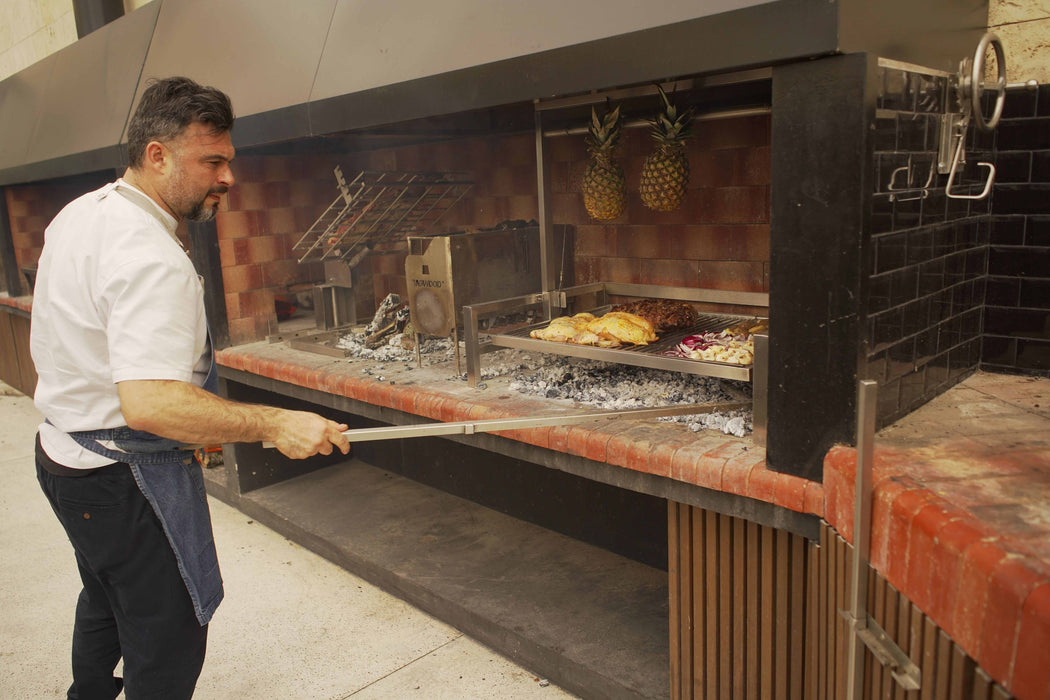 A chef cooking on a Tagwood insert grill in a brick parrilla