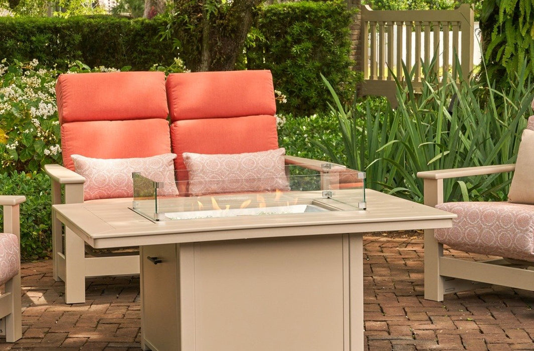 Telescope 36" x 54" fire table with the rectangular glass surround, flames lit, beside a coral cushioned loveseat