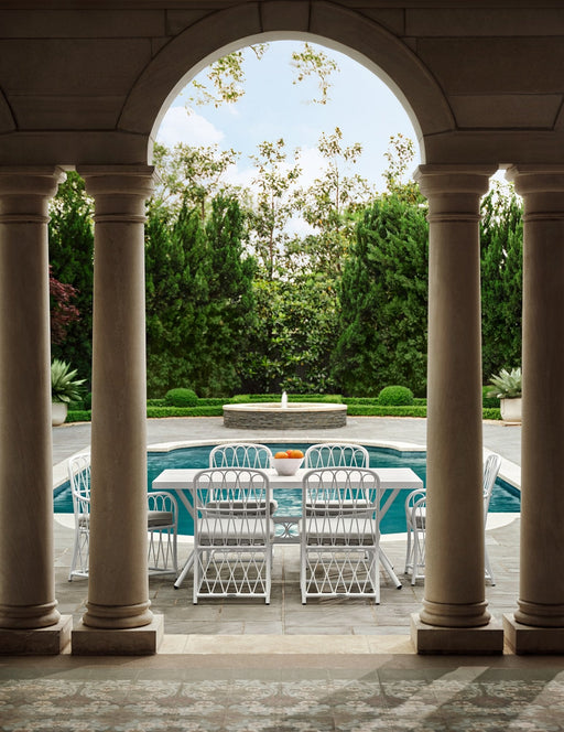 Woodard Cane dining set in White framed by stone arches beside a pool