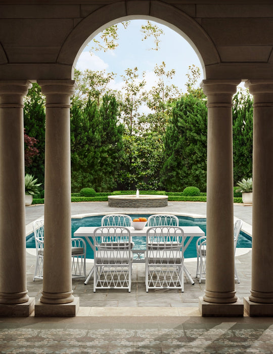 Woodard Cane dining set in White framed by stone arches beside a pool