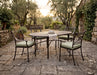 Woodard Hampton oval dining table on cabriole legs with four cushioned dining arm chairs in a stone courtyard