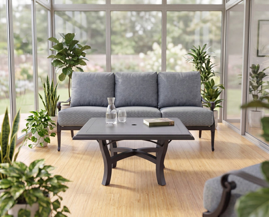 Woodard Solid Cast top square Carson base coffee table in front of a cushioned sofa in a sunroom