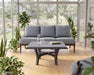 Woodard Solid Cast top square Carson base coffee table in front of a cushioned sofa in a sunroom